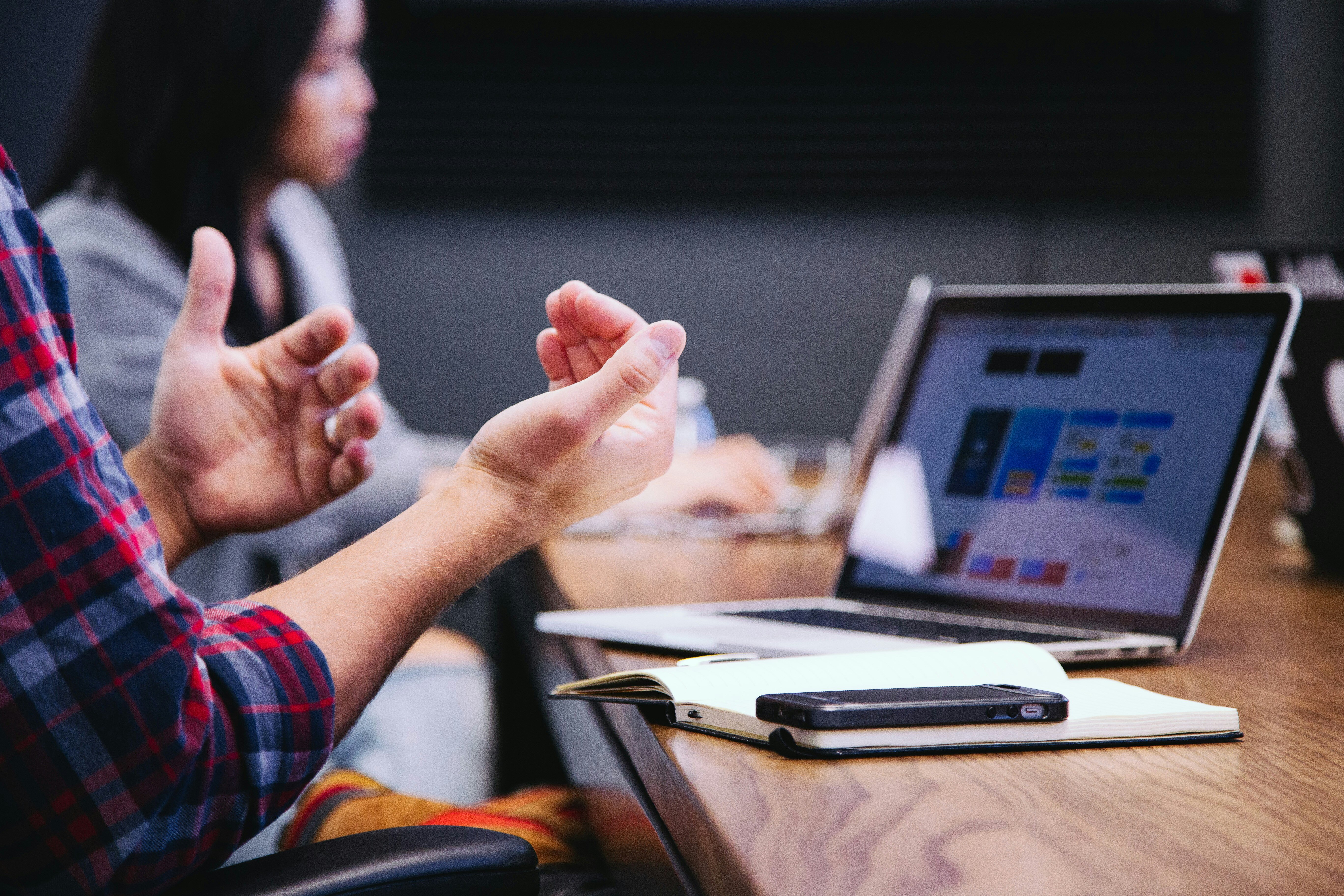 This photo is of a mans hands in an expressive posture next to a table with a laptop working