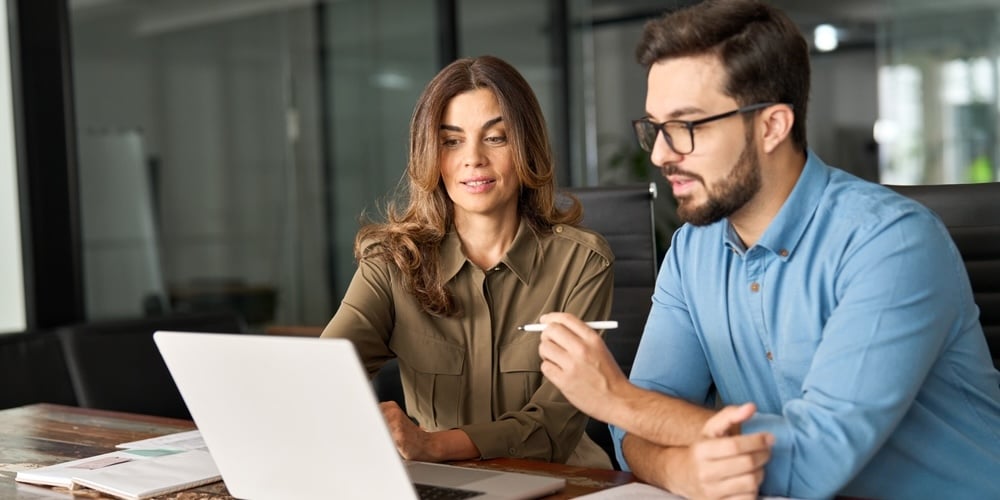 image of a man and a woman in an office both looking at an open laptop on a table